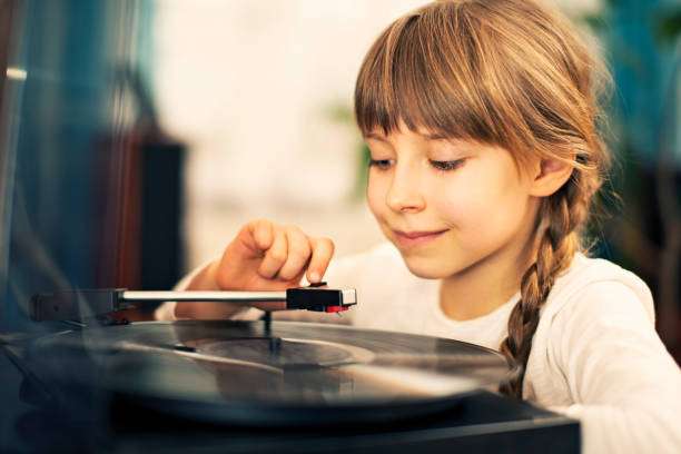 The little girl is listening to music on the vinyl record player.